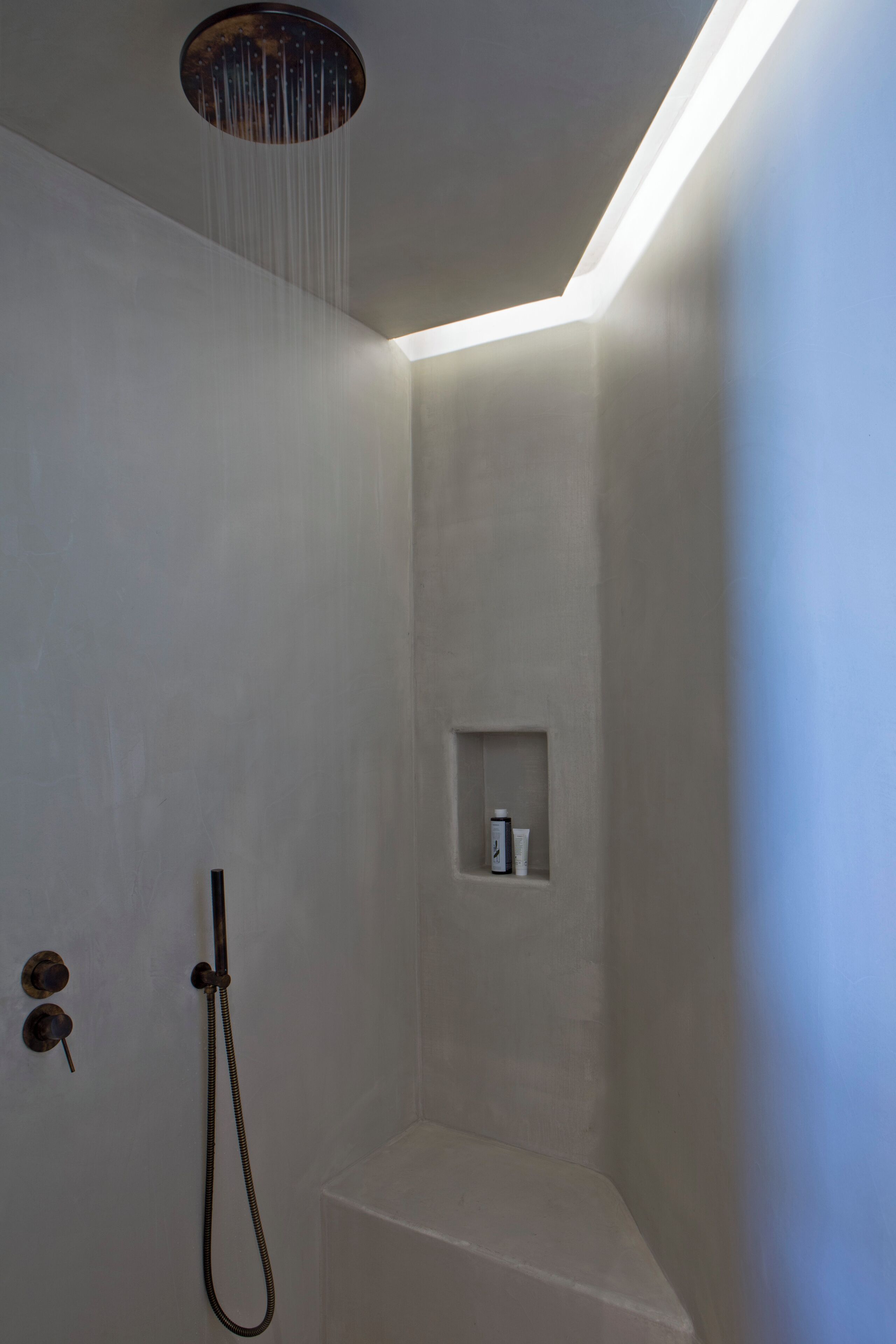 A modern shower with a curved ceiling, a built-in shelf, and a handheld showerhead.