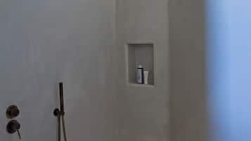 A modern shower with a curved ceiling, a built-in shelf, and a handheld showerhead.