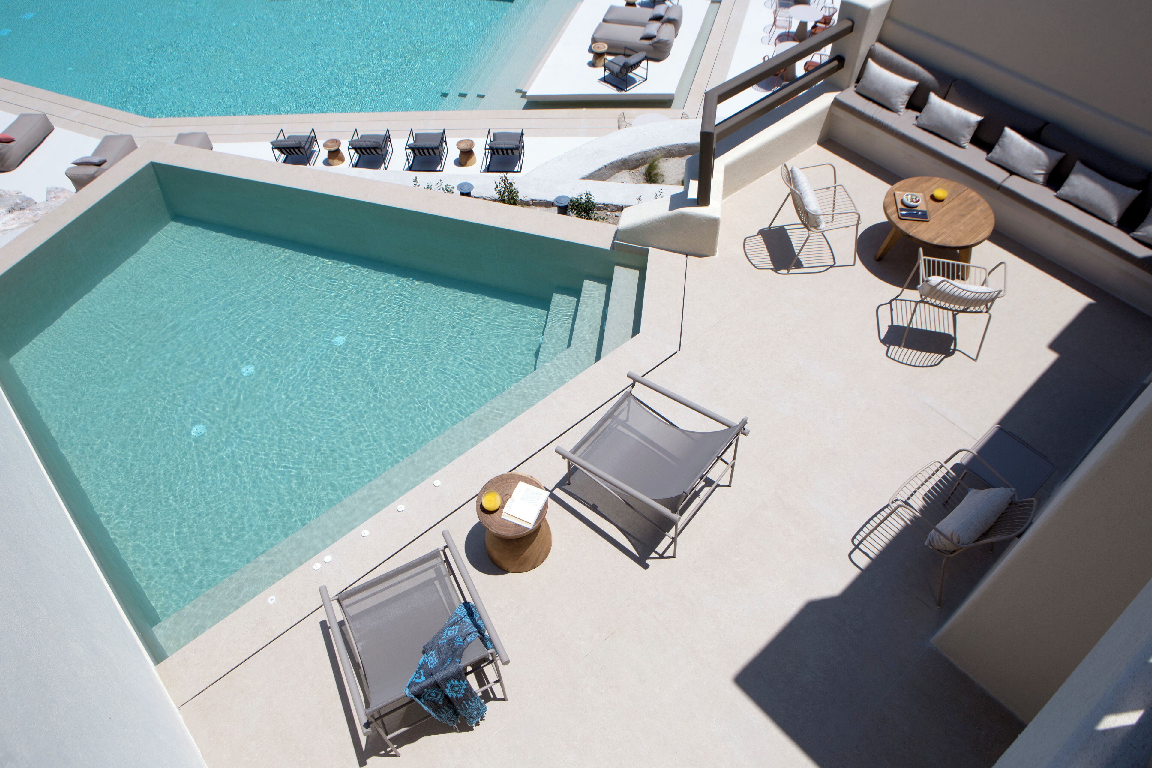An aerial view of a rooftop pool area with lounge chairs, a small table, and a sofa.