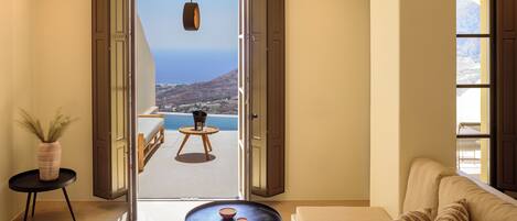 A room with a sofa, a small round table, a potted plant, and a view of a balcony with a table and chairs.