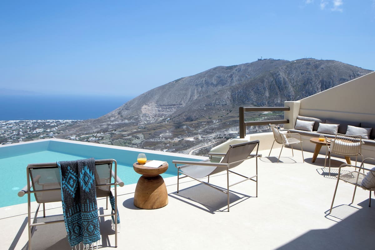 A poolside area with lounge chairs, a wooden table with a towel, and a view of a mountainous landscape.