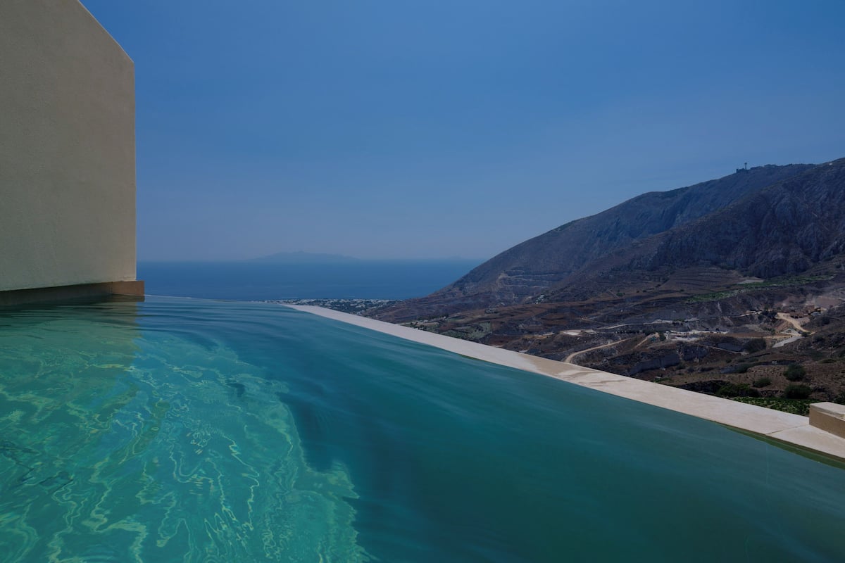 A pool with clear blue water, a mountainous landscape, and a clear sky.