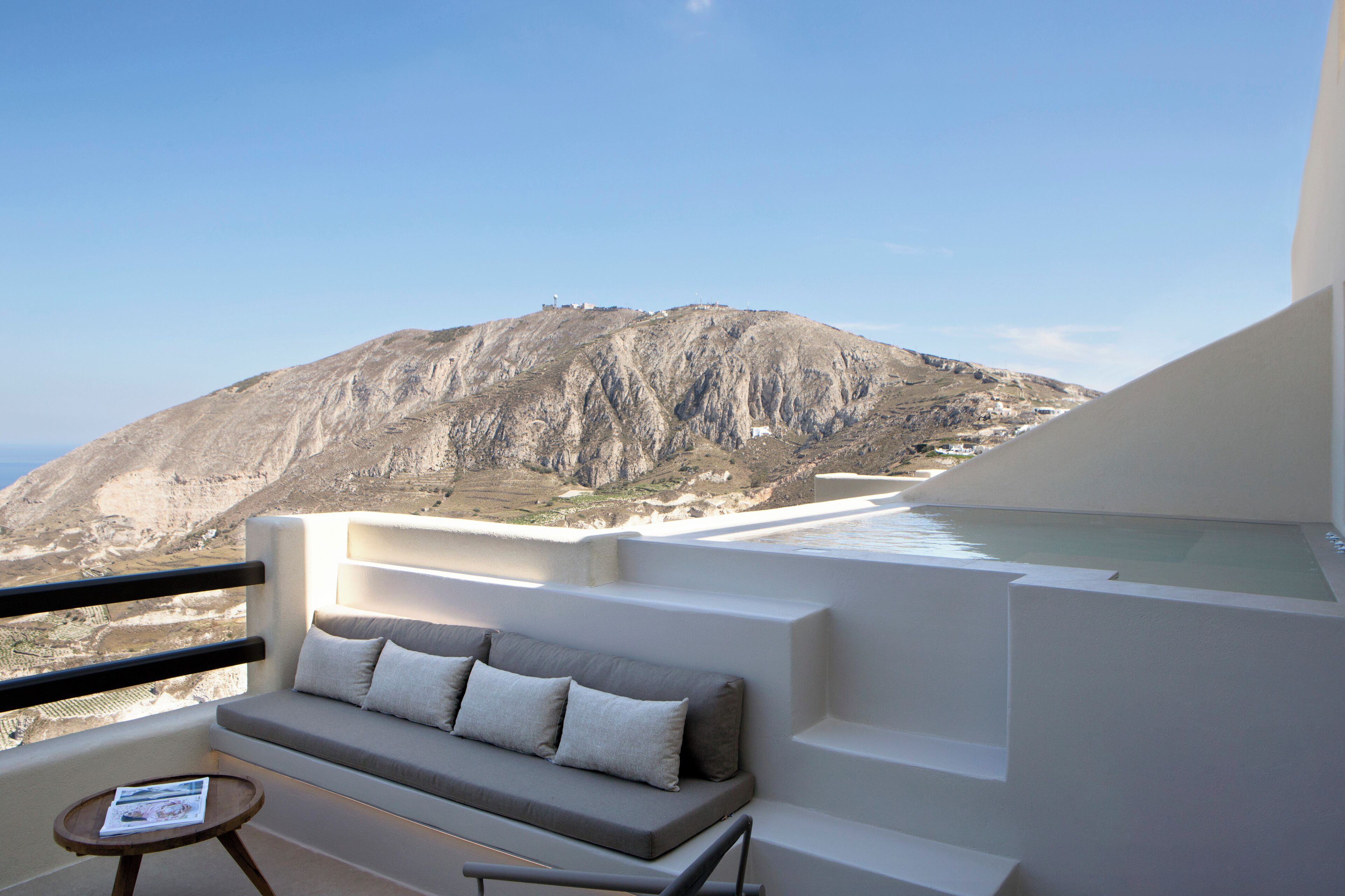 A balcony with a sofa and a small table, overlooking a mountainous landscape.