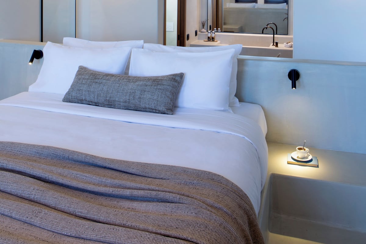 A modern hotel room with a large bed, a nightstand, a mirror, and a bathroom visible through an open door.