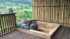 A wooden hot tub on a deck with a bamboo backdrop and a view of a lush landscape. - The Onsen Hot Spring Resort (Batu)