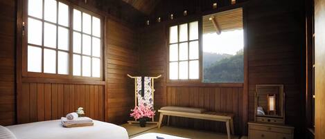 A wooden cabin room with two beds, a bench, a dresser, and large windows.
