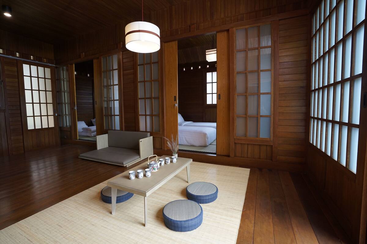 Um quarto tradicional japonês com tatames, uma mesa baixa com conjunto de chá e portas de correr com painéis de vidro.