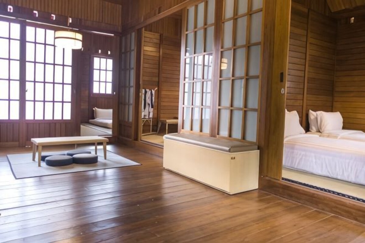 Una habitación de estilo japonés tradicional con suelo de tatami, una cama baja de madera, un banco y una puerta corredera con paneles de vidrio.