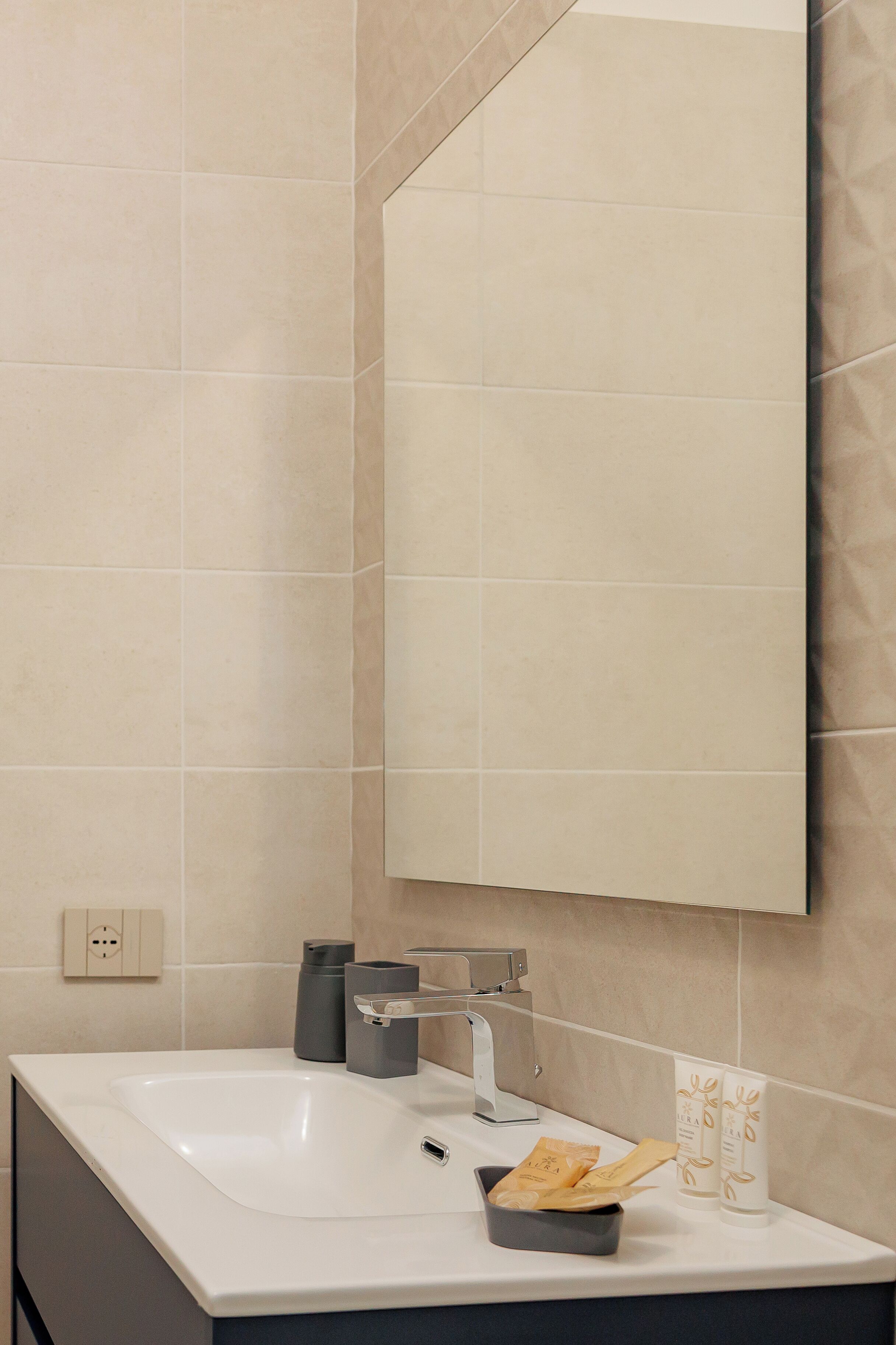A modern bathroom with a white sink, a large mirror, and a towel rack.