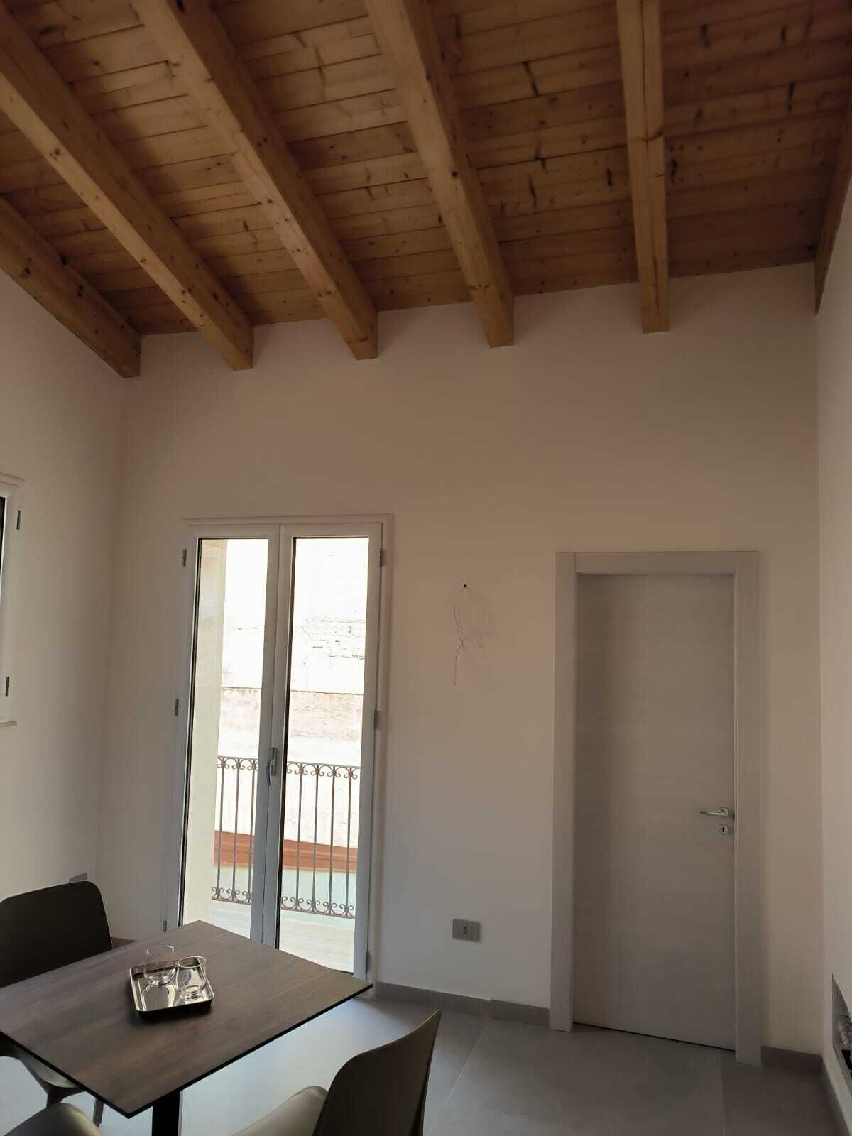 Ein Zimmer mit Holzboden, einem Esstisch mit Stühlen, einer Schiebetür aus Glas und einer geschlossenen Tür.