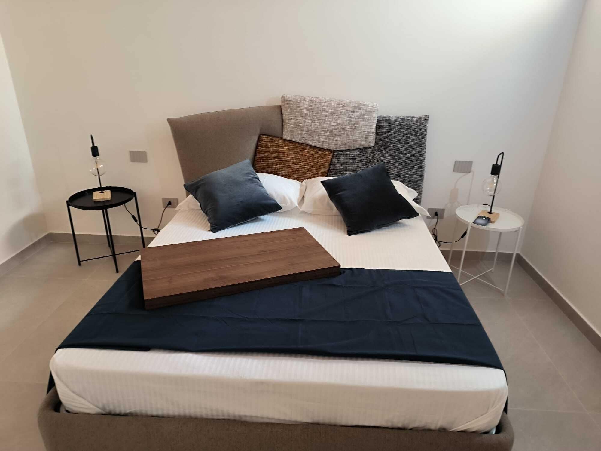 A neatly made bed with a wooden headboard, two bedside tables, and a small round table with a lamp.
