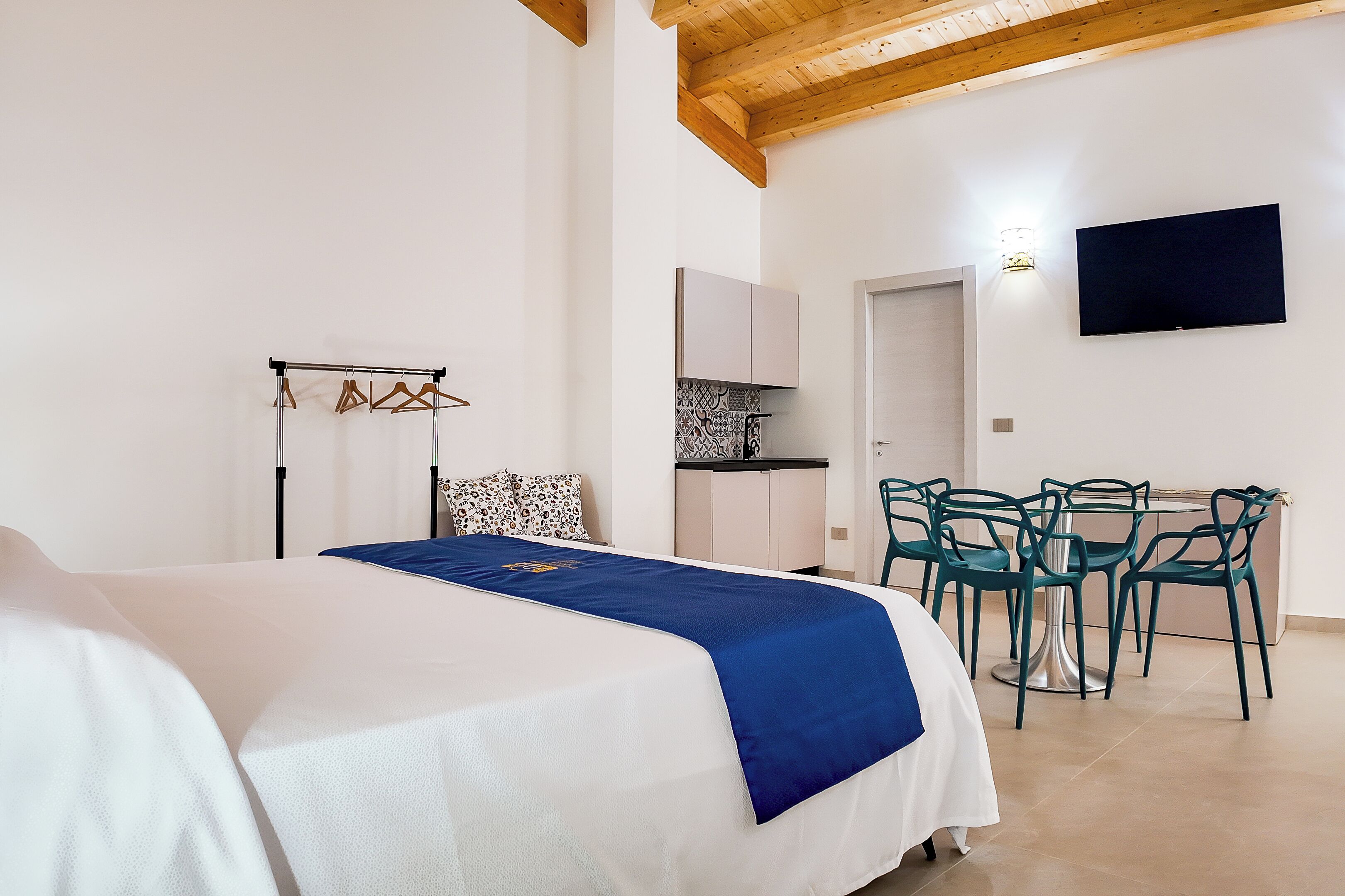 Une chambre avec un lit, un bureau et une chaise. Un téléviseur est fixé au mur et il y a un étendoir à linge.