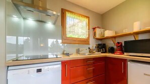 A compact kitchen with a dishwasher, red cabinets, a window with a view, and a coffee maker.