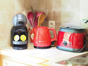 Una encimera de cocina con una cafetera, un hervidor eléctrico rojo y un tostador.