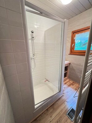 Zona de ducha con puerta de cristal, paredes de azulejos y suelo de madera.