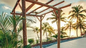 Ein Poolbereich mit Pergola, umgeben von Palmen und Blick auf das Meer.