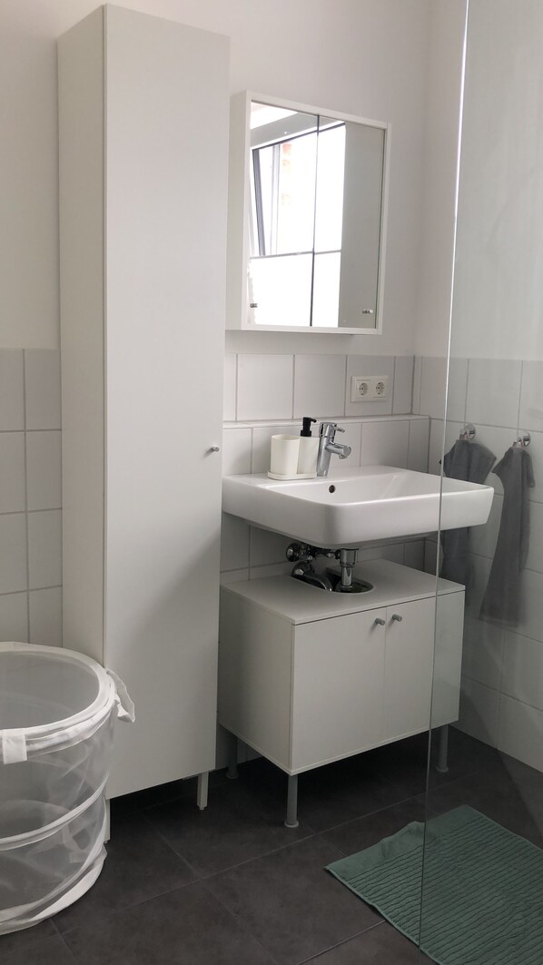 A bathroom with a white sink, a mirror above it, and a shower area.