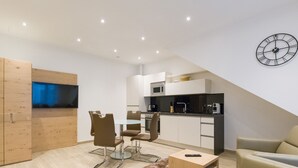 A modern kitchen with a microwave, stove, and coffee maker. There is a dining area with a table and chairs, and a TV mounted on a wooden cabinet. - Stadtwohnung mit Flair 1200 (Vienna)