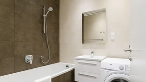A modern bathroom with a bathtub, a shower, a sink, and a washing machine. - Stadtwohnung mit Flair 1200 (Vienna)