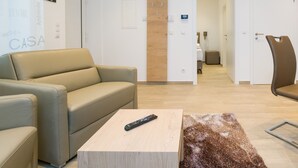 A modern hotel lobby with a beige sofa, a wooden coffee table, and a remote control on it. There is a wooden door with a sign above it, and a hallway leading to a bedroom. - Stadtwohnung mit Flair 1200 (Vienna)