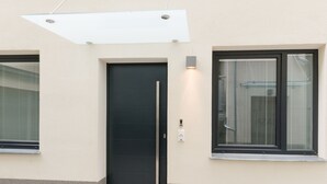 A modern building facade with a black door, two windows with blinds, and a recessed light fixture. - Stadtwohnung mit Flair 1200 (Vienna)
