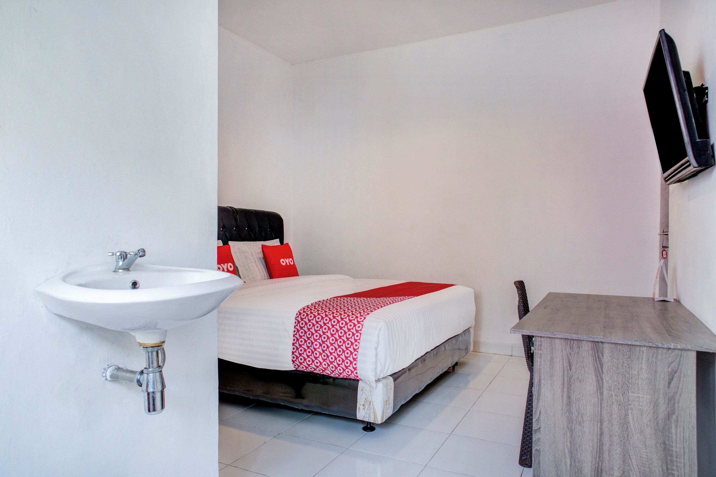 A bedroom with a bed, a bedside table, a sink, and a mirror.