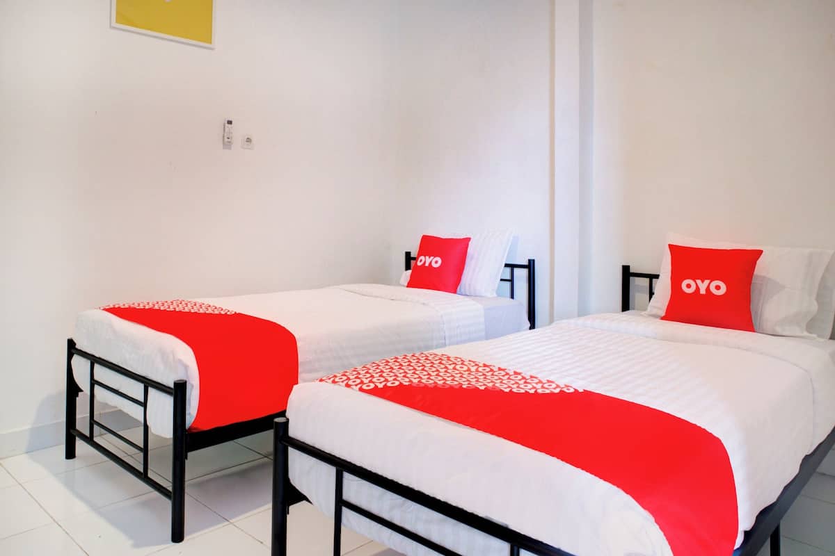 A hotel room with two single beds, each with a red and white bedspread and matching pillows.