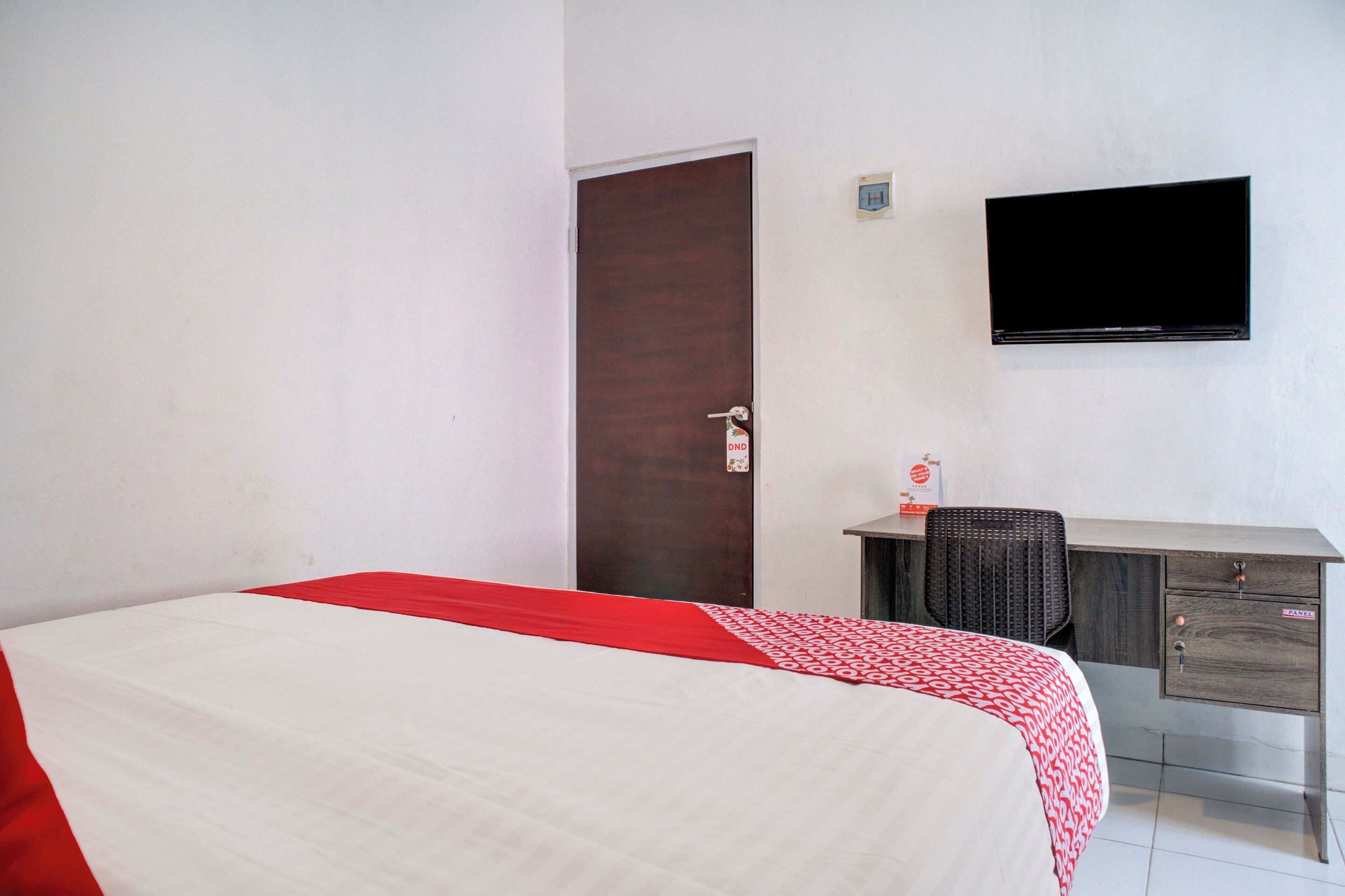 A hotel room with a bed, a desk, a chair, and a TV on the wall.