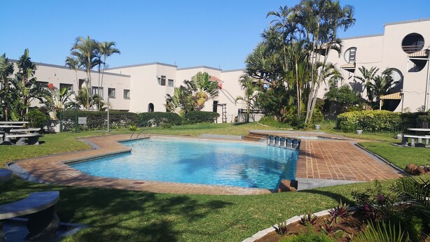 A swimming pool surrounded by a well-maintained lawn, palm trees, and a building with a modern design.