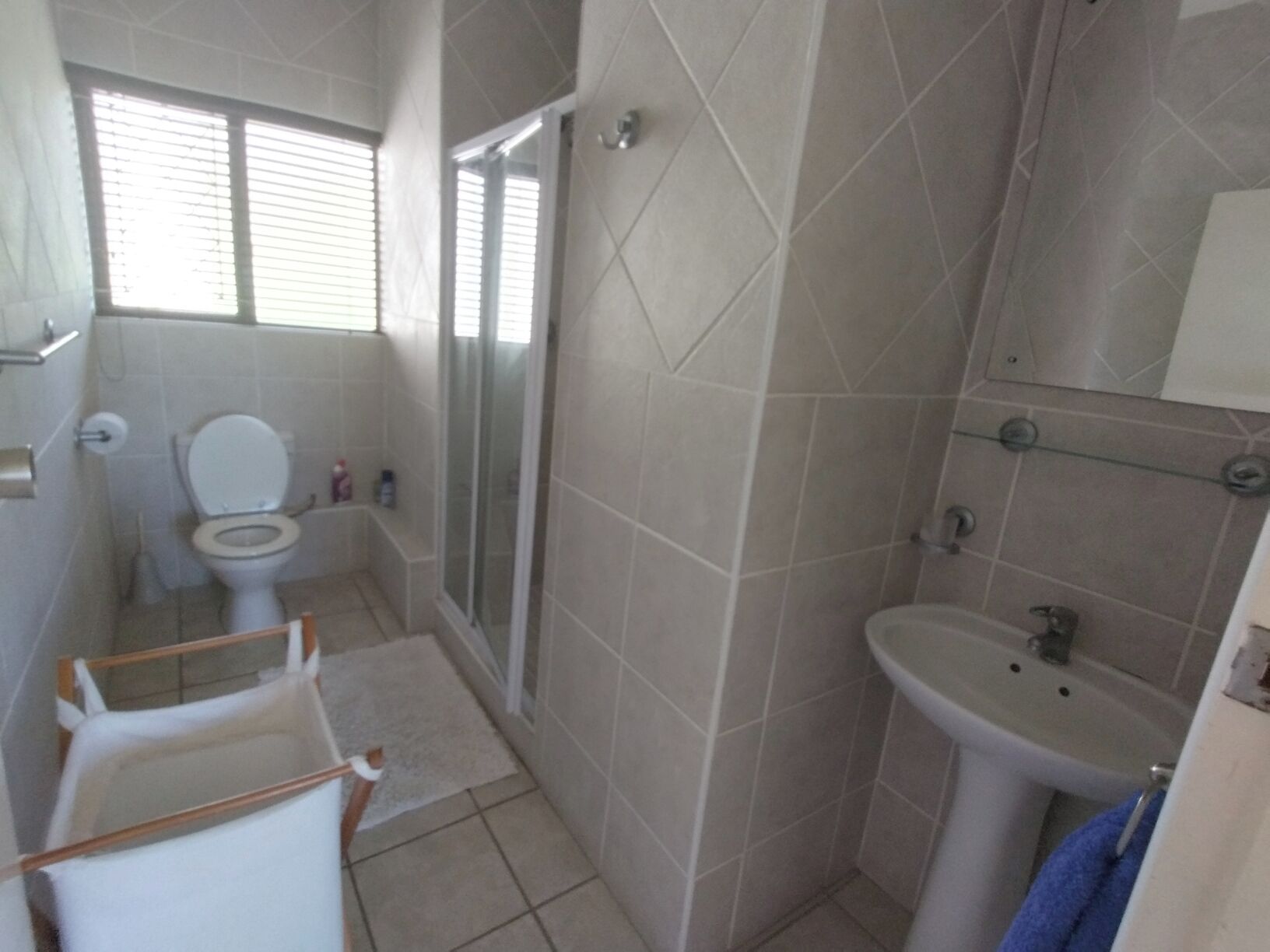 Casa de banho com sanita, chuveiro, lavatório e janela com estores.