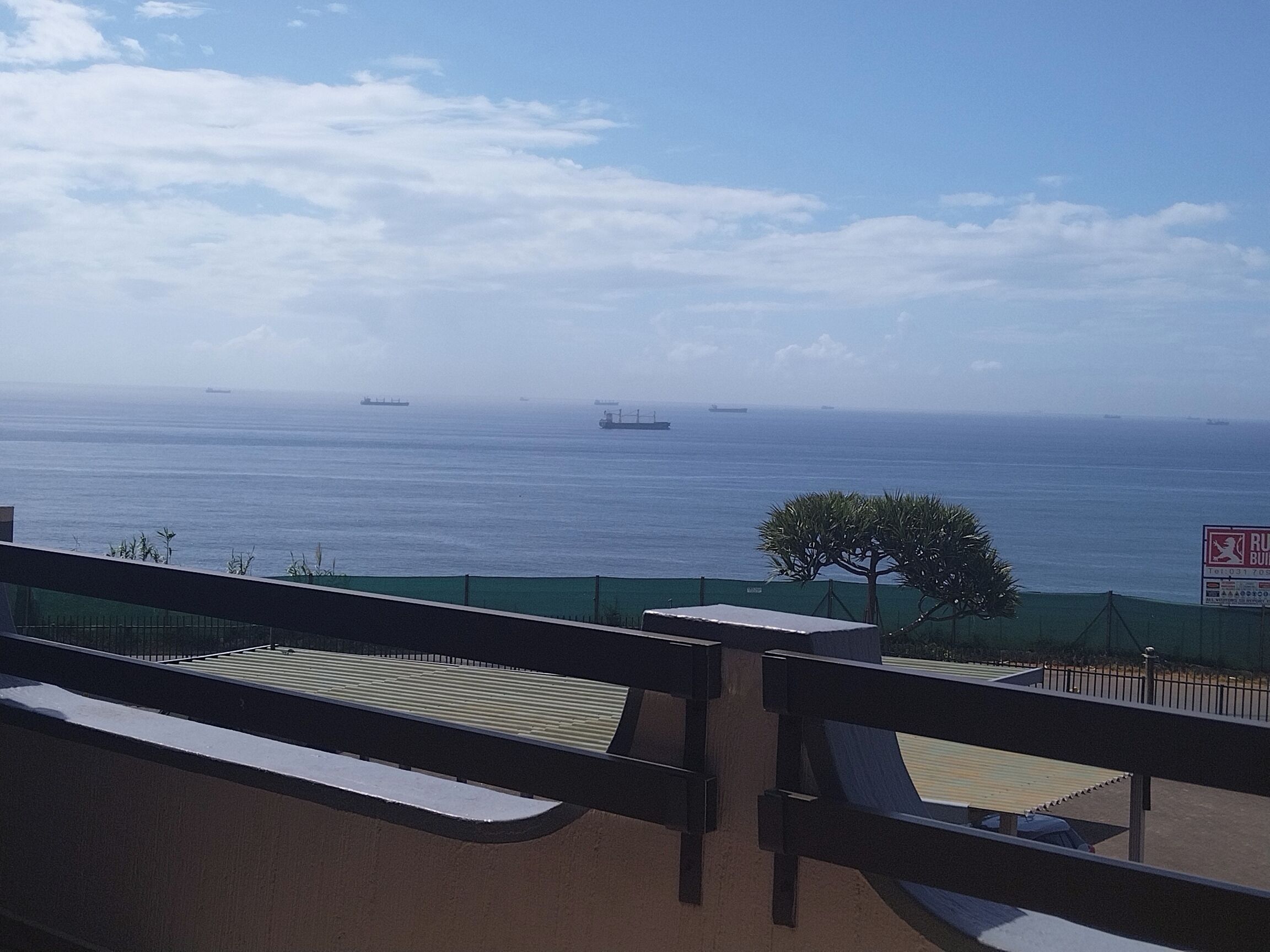 A balcony with a view of the sea and ships. There is a sign for a building rental service.