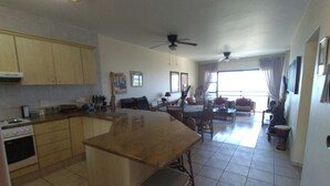 A spacious kitchen with a central island, a dining area with a table and chairs, and a living room with a sofa and a TV.