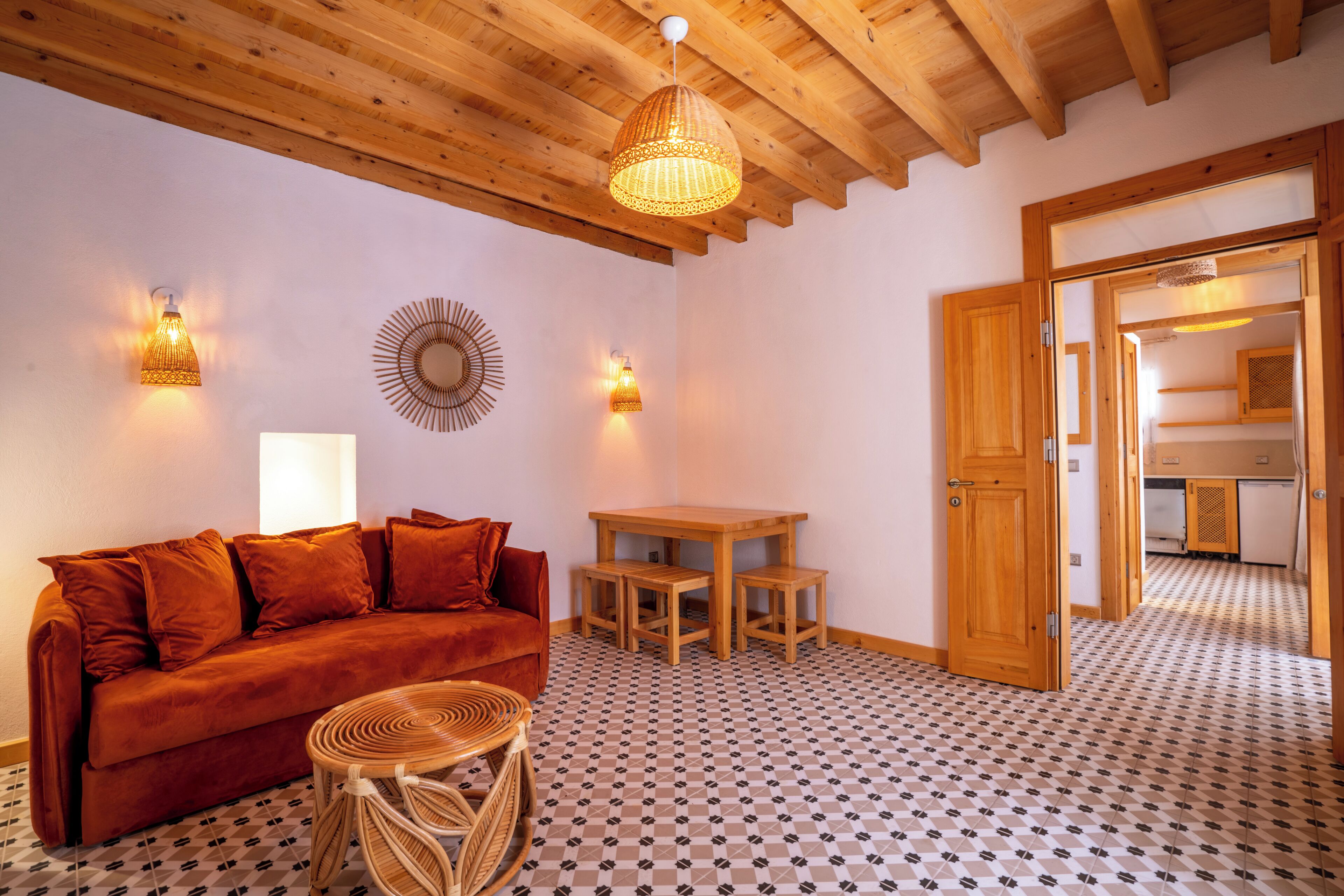 A cozy room with a wooden ceiling, a red sofa, a small round table, and a patterned floor.