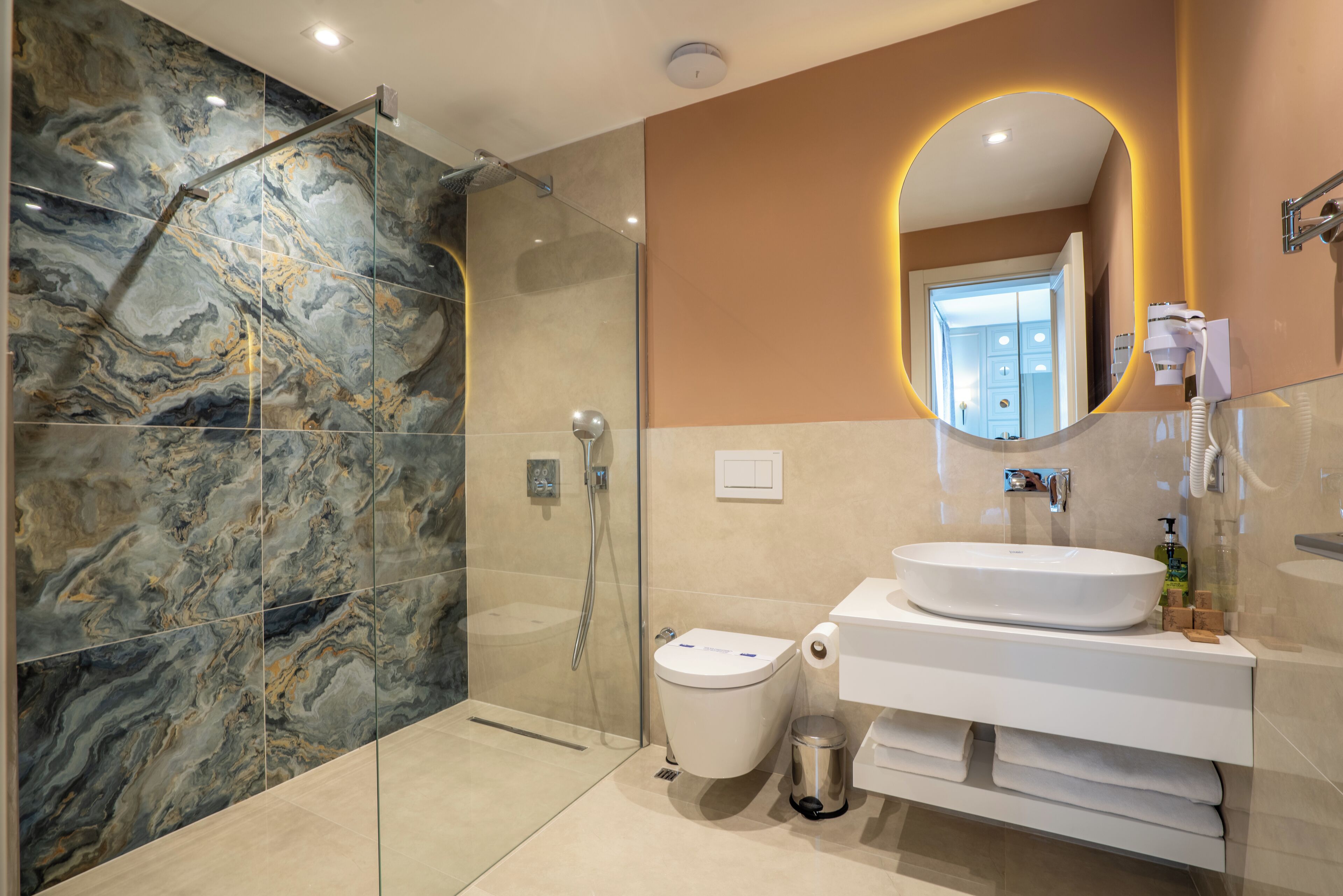 A modern bathroom with a glass-enclosed shower, a white sink, and a marble-tiled wall.