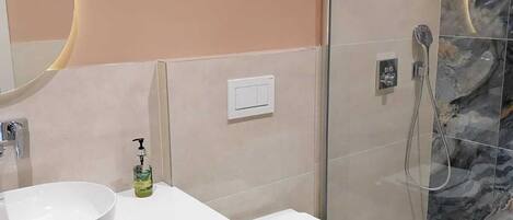 A modern bathroom with a large white sink, a toilet, and a glass-enclosed shower.