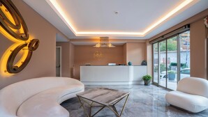 A modern lobby with a reception desk, seating area, and large windows offering a view of the outdoors. - Muhtar Hotel (Kas)
