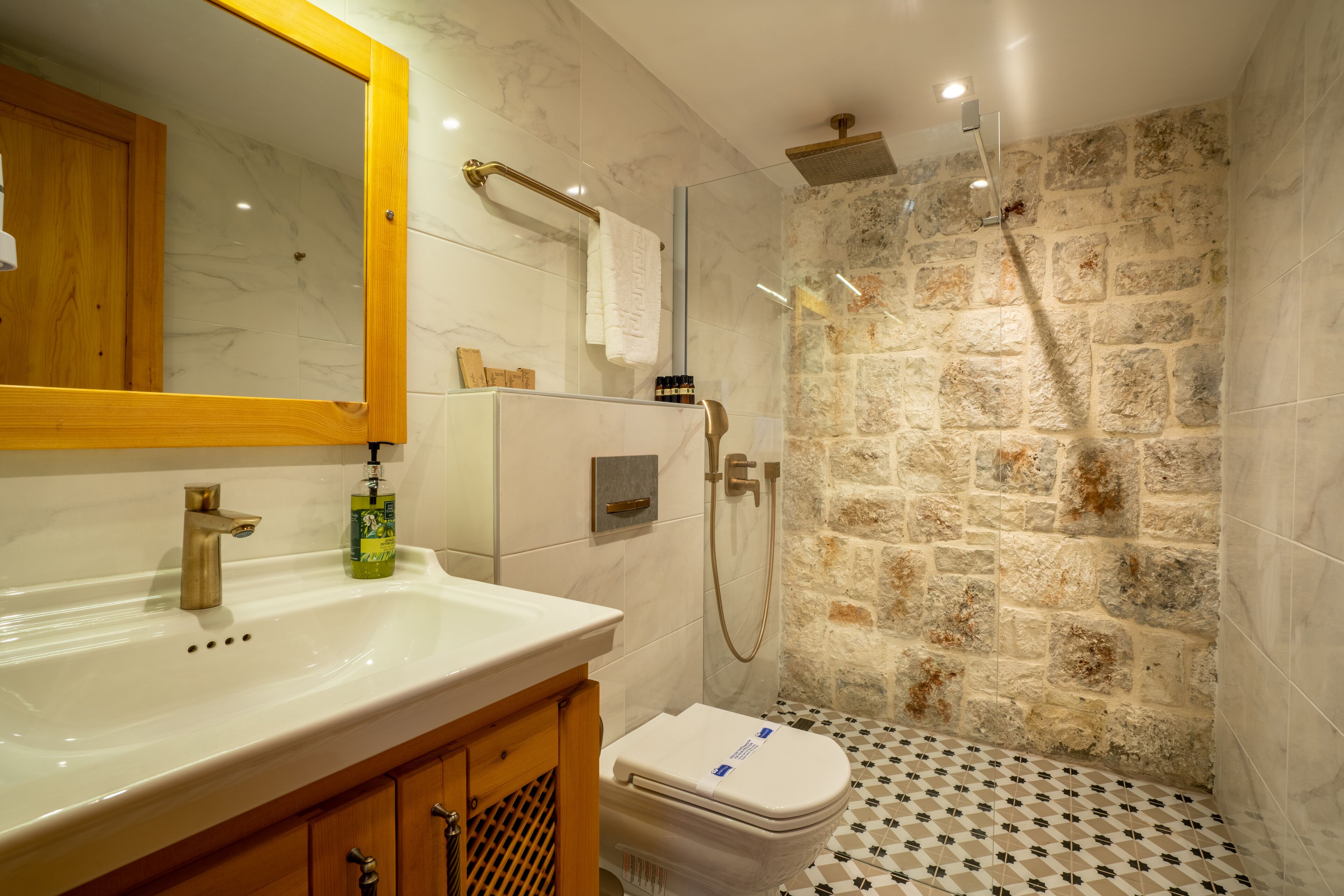 A bathroom with a marble sink, a wooden cabinet, a toilet, and a shower with a stone wall.