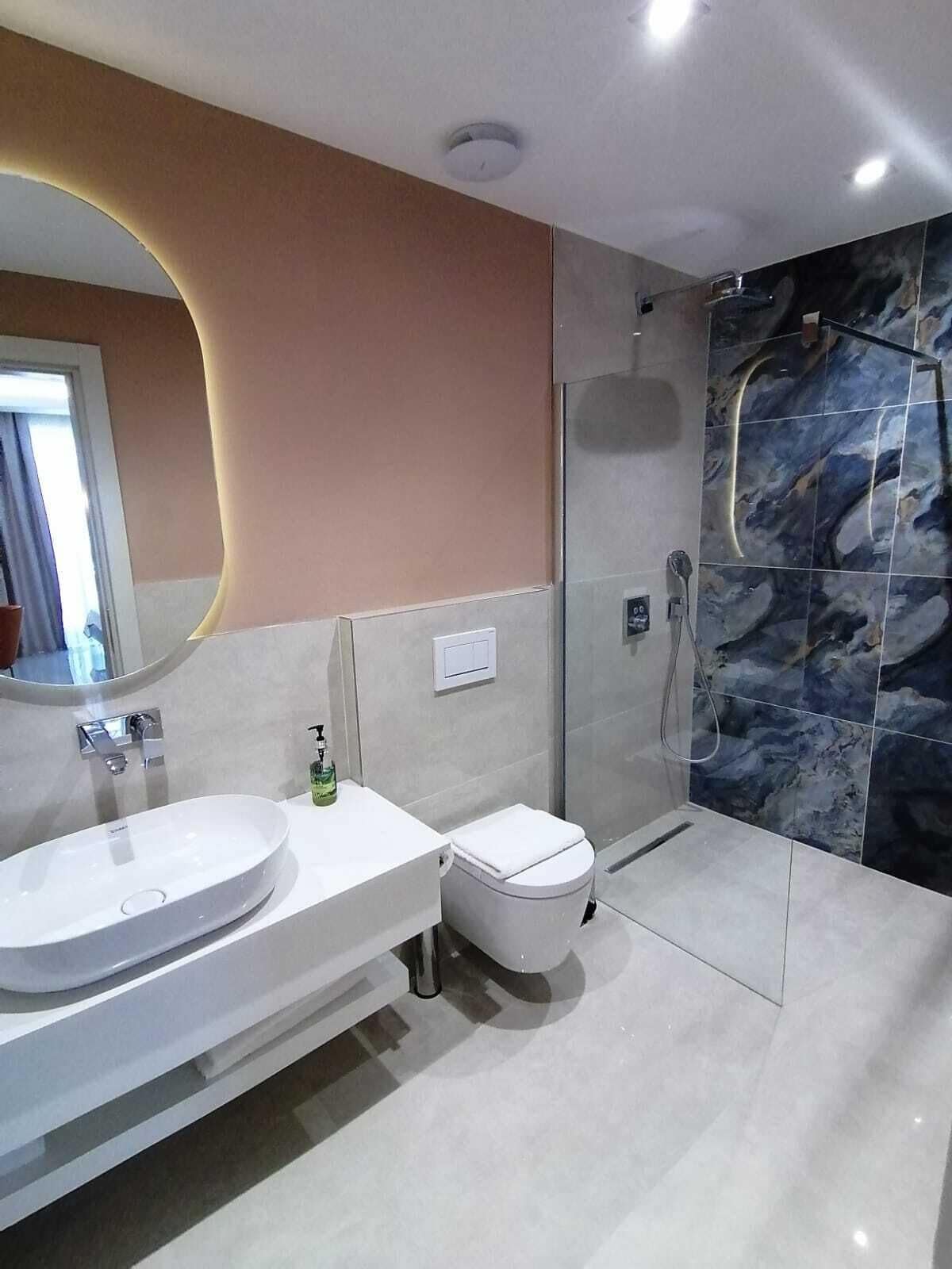 Un baño moderno con un lavamanos grande de color blanco, un inodoro y una zona de ducha con mampara de vidrio.