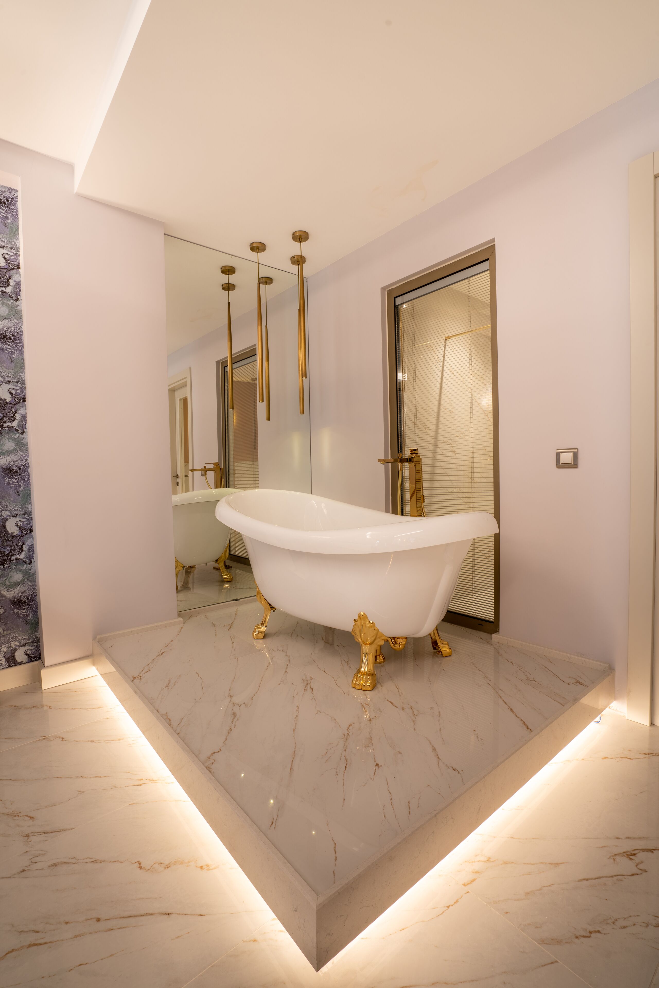 A modern bathroom with a freestanding bathtub, marble flooring, and gold fixtures.