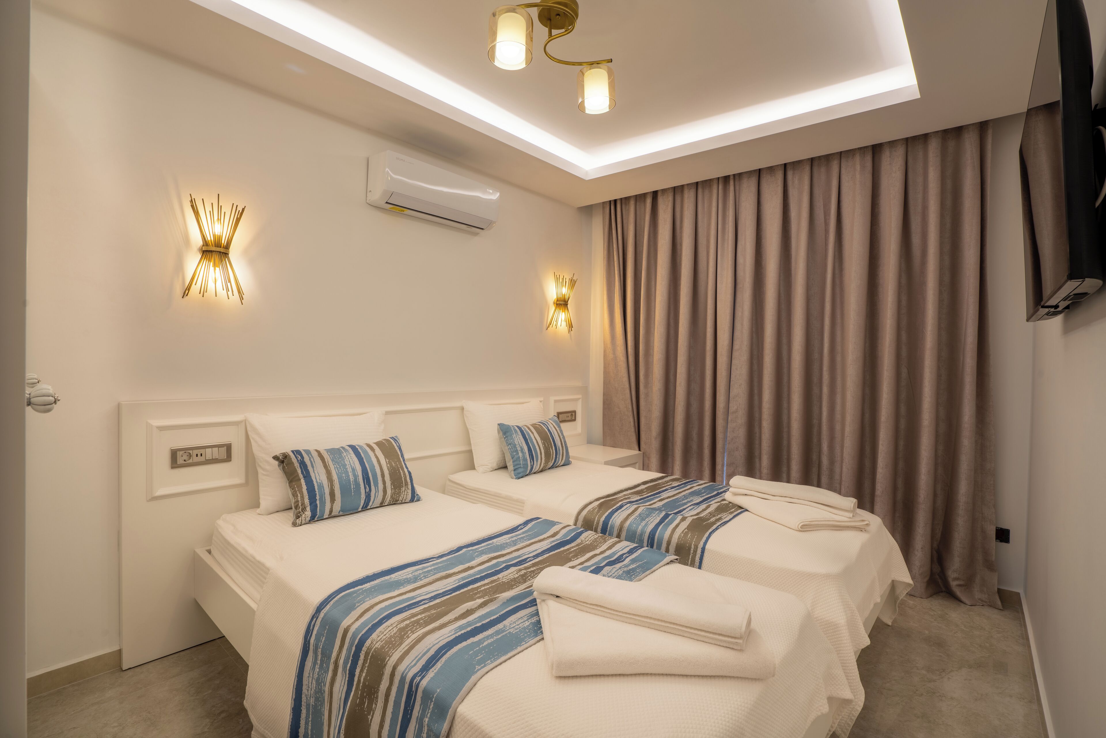 A hotel room with two beds, a ceiling light fixture, an air conditioner, and a TV mounted on the wall.