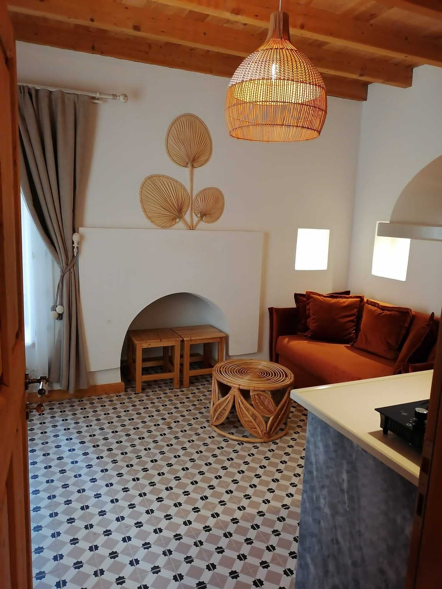 A cozy living room with a patterned floor, a wooden ceiling, a woven light fixture, a sofa, and a small table.