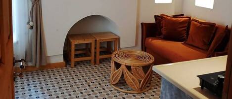 A cozy living room with a patterned floor, a wooden ceiling, a woven light fixture, a sofa, and a small table.