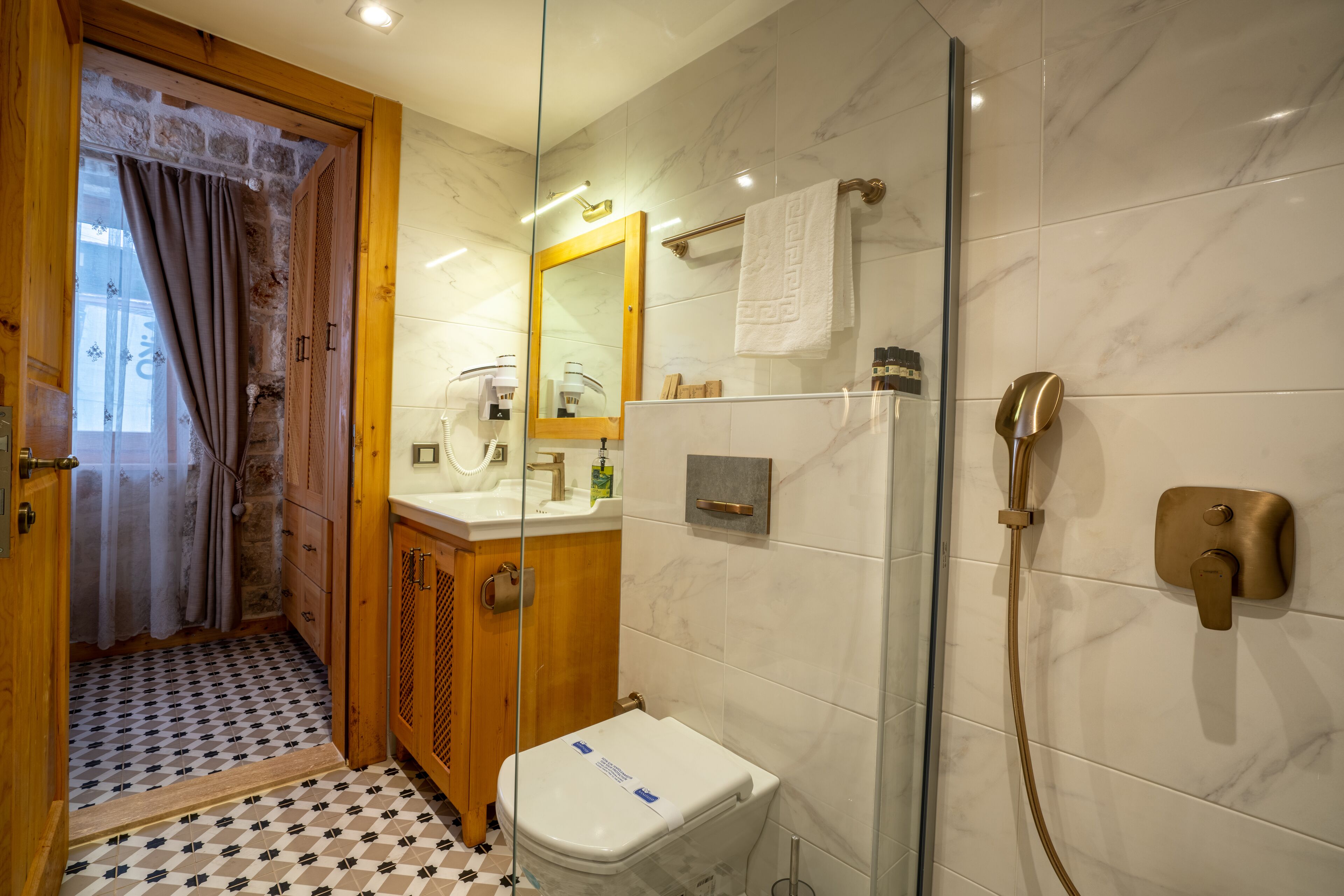 Une salle de bain comprenant des toilettes, un lavabo, un miroir, un porte-serviettes, une douche et une porte en verre donnant sur l’espace de la douche.