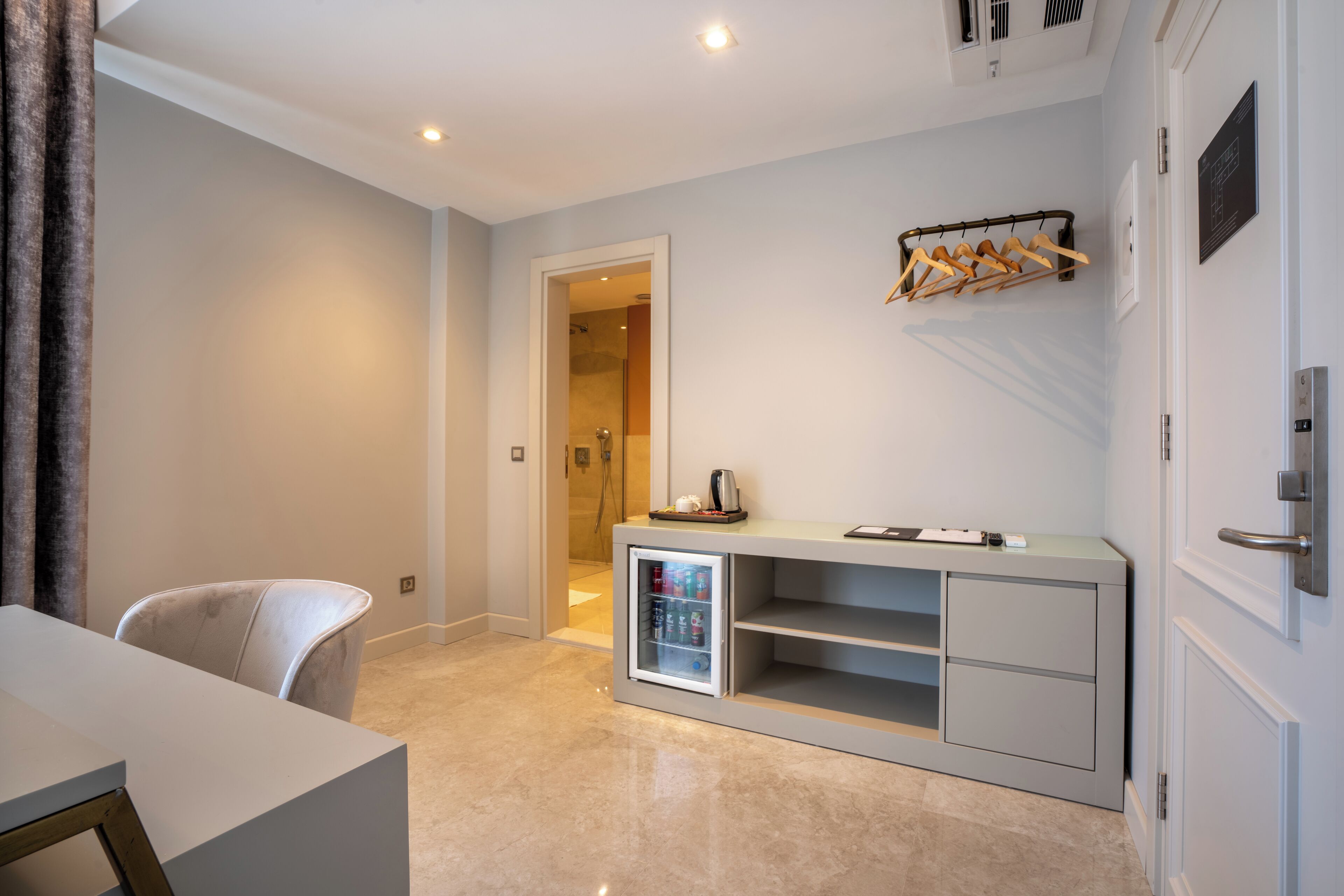 Een moderne hotelkamer met een minimalistisch design, voorzien van een wit bureau, een zithoek, een minibar en een kapstok.