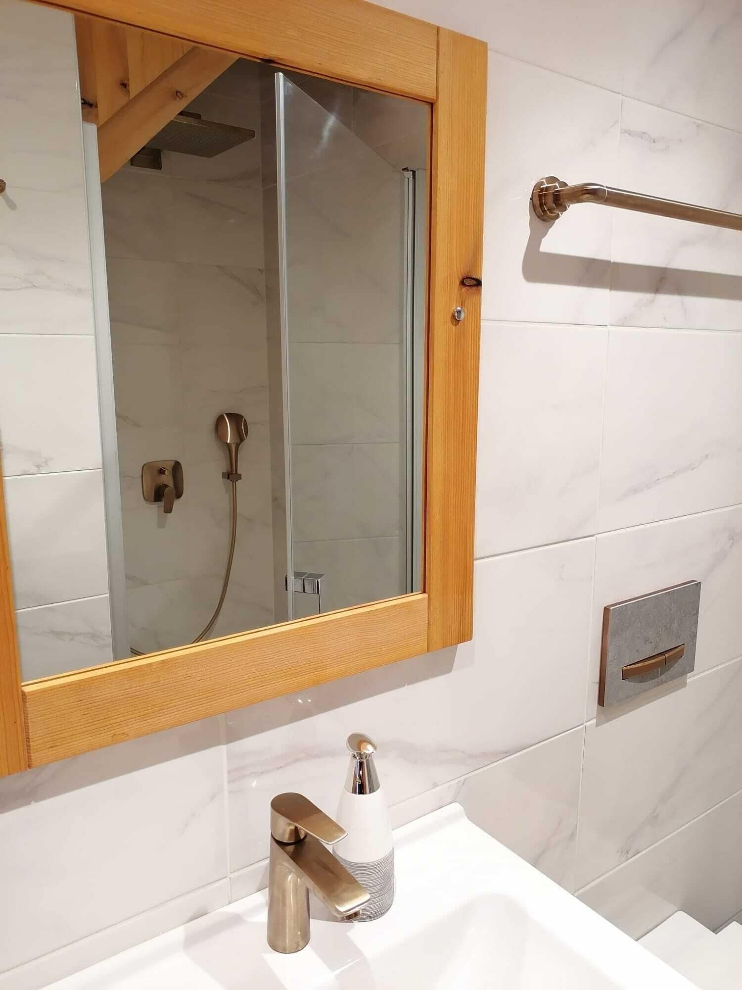 A bathroom with a wooden-framed mirror, a white sink with a modern faucet, and a glass shower enclosure.