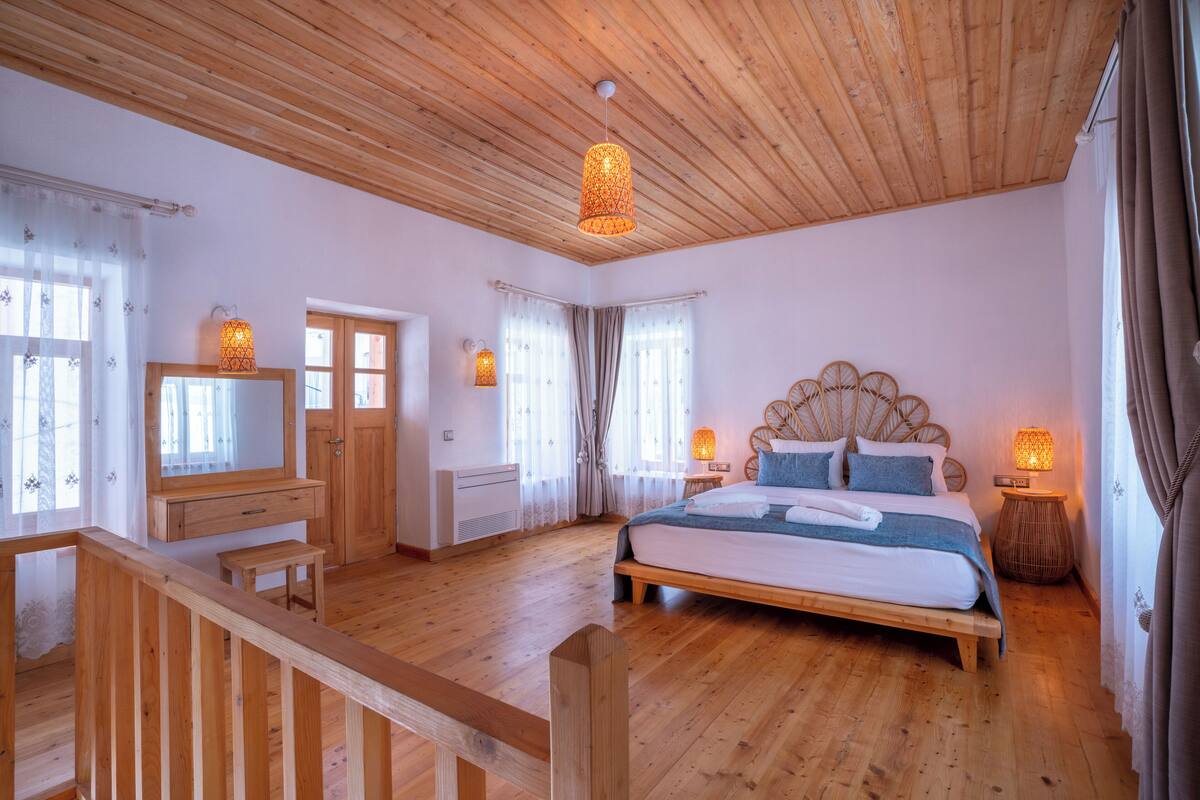 A wooden-floored bedroom with a bed, bedside lamps, a mirror, and a wooden bench.