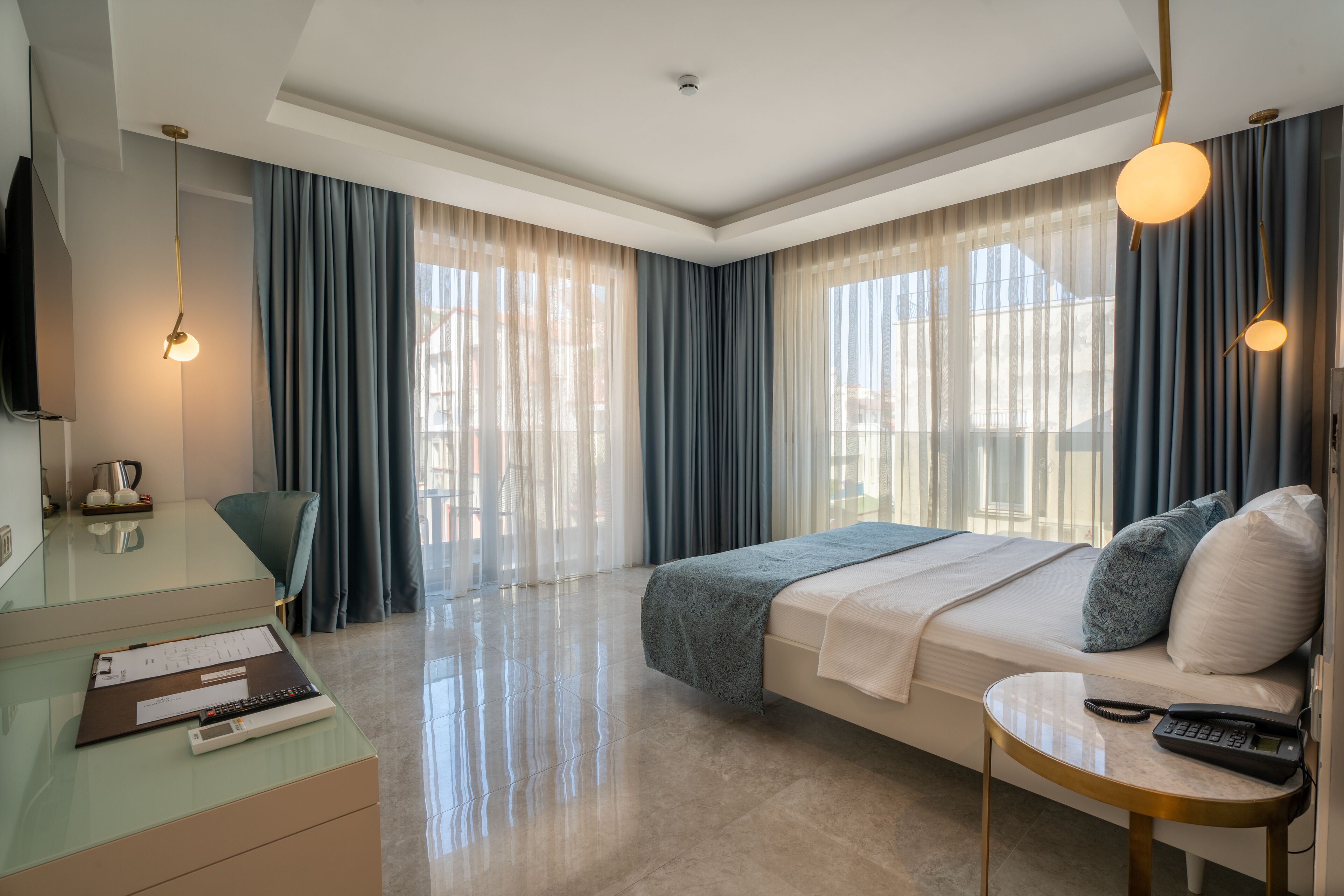 A modern hotel room with a bed, a desk with a chair, a TV, and a large window with curtains.
