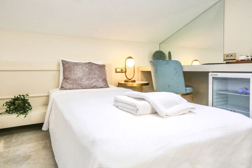 A hotel room with a neatly made bed, a bedside lamp, a chair, and a small refrigerator.