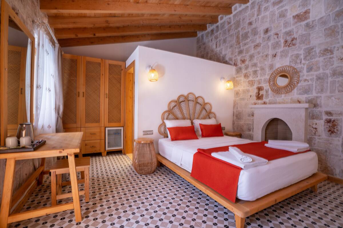A bedroom with a wooden bed, a small table, a chair, and a decorative mirror on the wall.