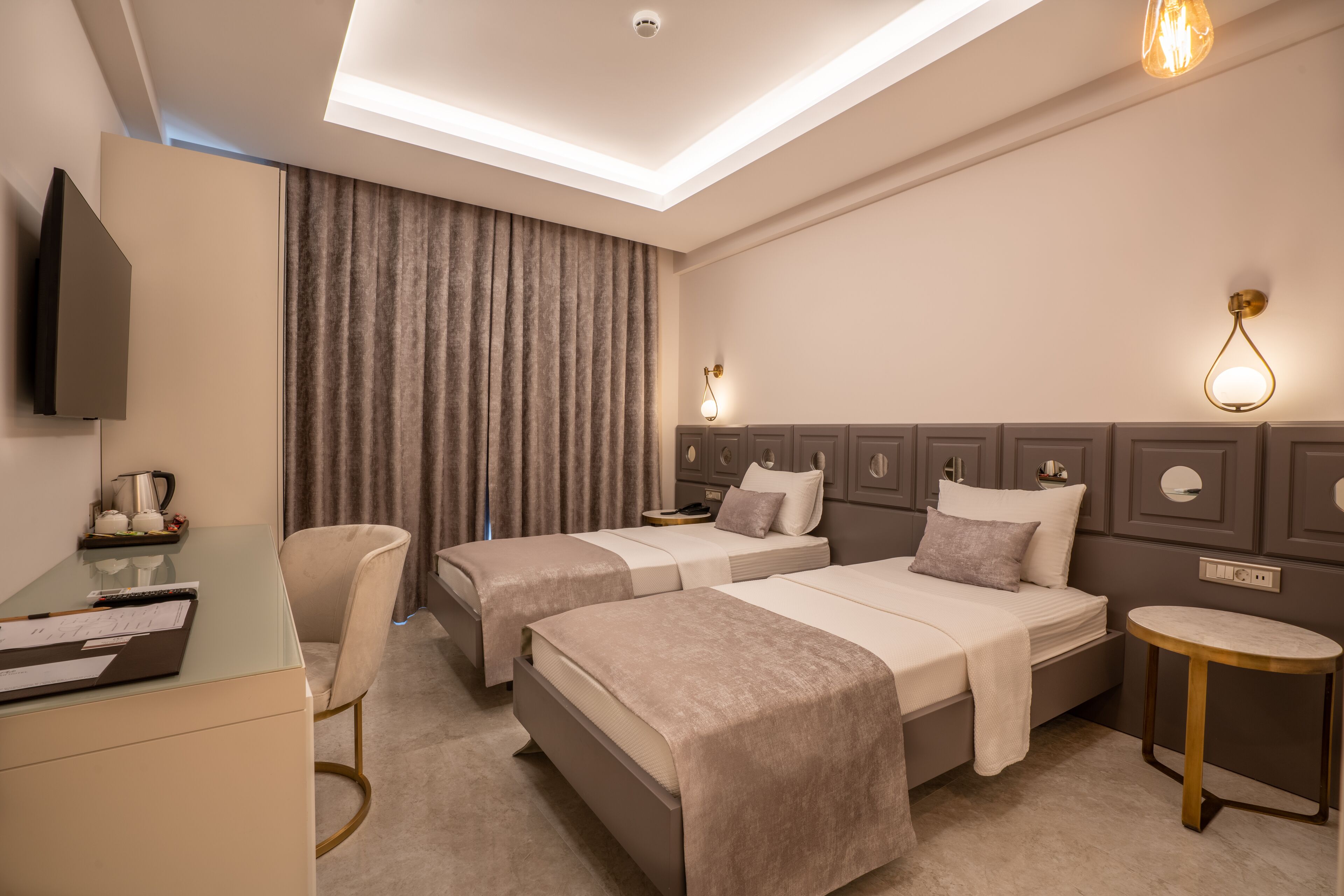A hotel room with two beds, a desk, a chair, a round table, and a TV.